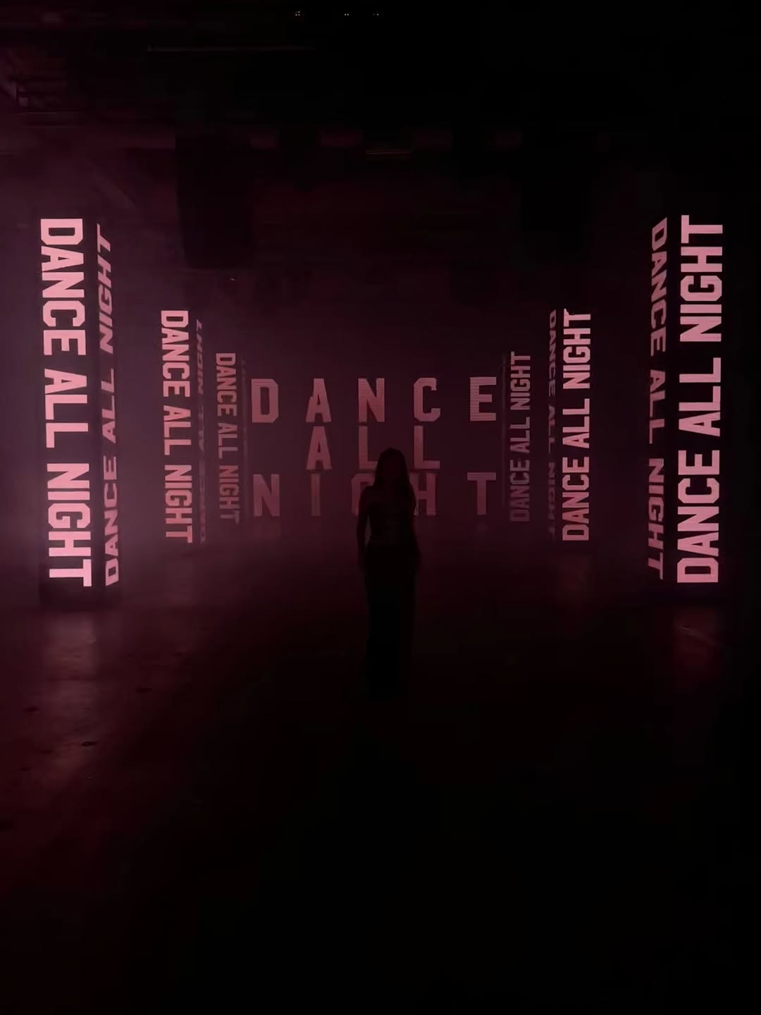 A silhouette in a dark room surrounded by glowing pink panels reading Dance All Night