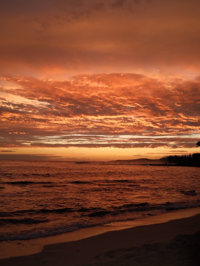 Burning orange sunset clouds over dark waves and wet sand